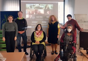 Das Bild zeigt die Teilnehmer:innen der BAG-Sitzung in Präsenz und dahinter die digital zugeschalteten.